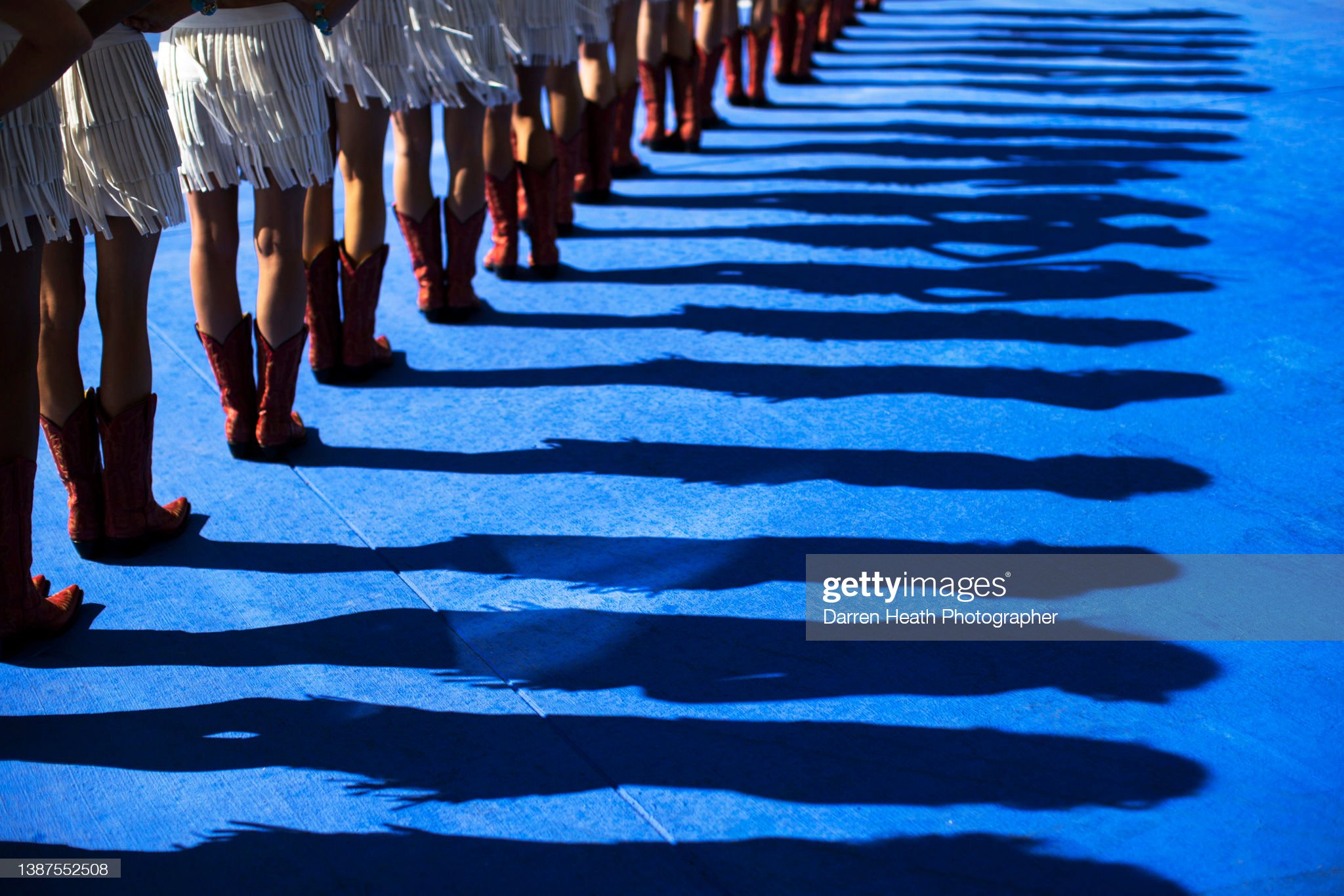 The shadows thrown by cowgirl outfit and cowboy boots wearing grid girls standing in a line in the pit lane during the Formula One drivers' parade at the 2013 United States Grand Prix.
