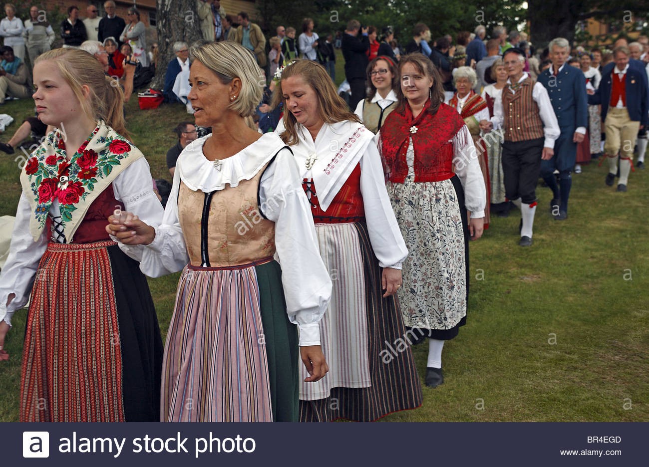 Couples in traditional Swedish folk costumes parade at midsummer celebration.