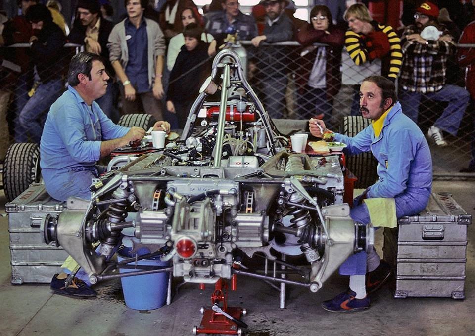 Two Ferrari mechanics eat on an F1 car.
