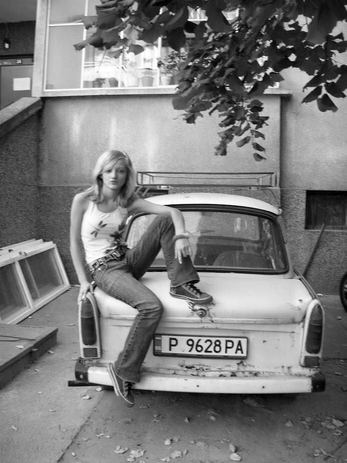 A young girl on the rear hood of a Trabant.