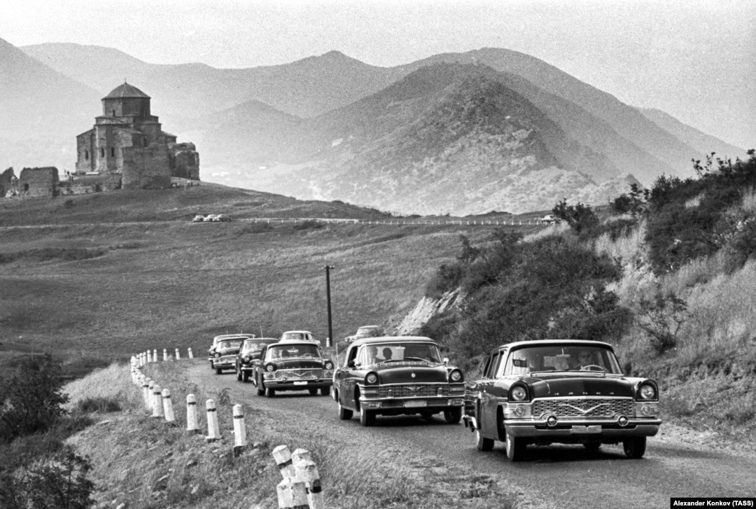 A convoy of Soviet Chaika cars glide along a road near Tbilisi, Georgia. 