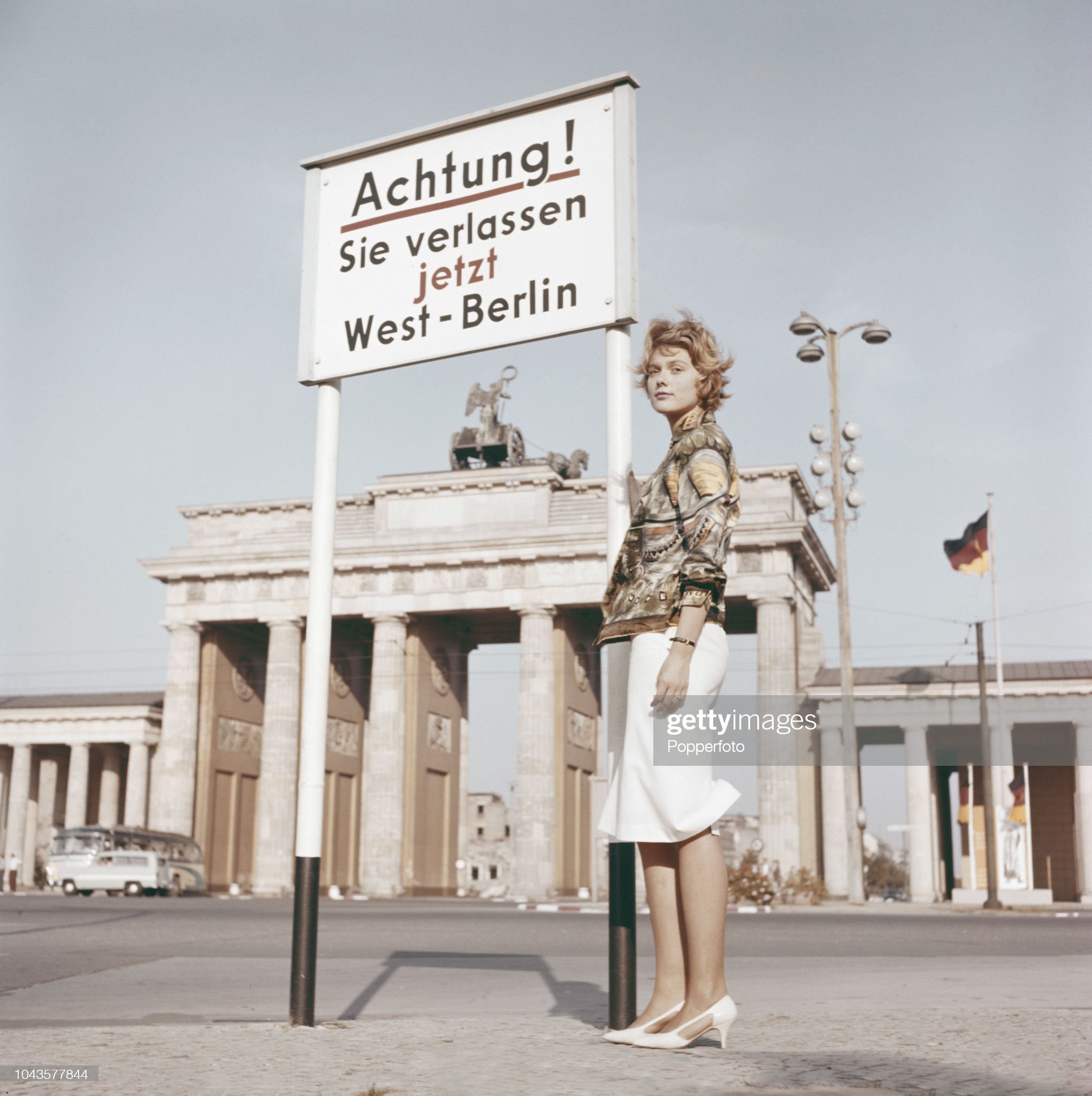 View from the Tiergarten of a young woman standing beside a warning sign in front of the Brandenburg Gate at the border between the British Sector of West Berlin and the Soviet Sector of East Berlin in the divided city of Berlin in East Germany in October 1960.