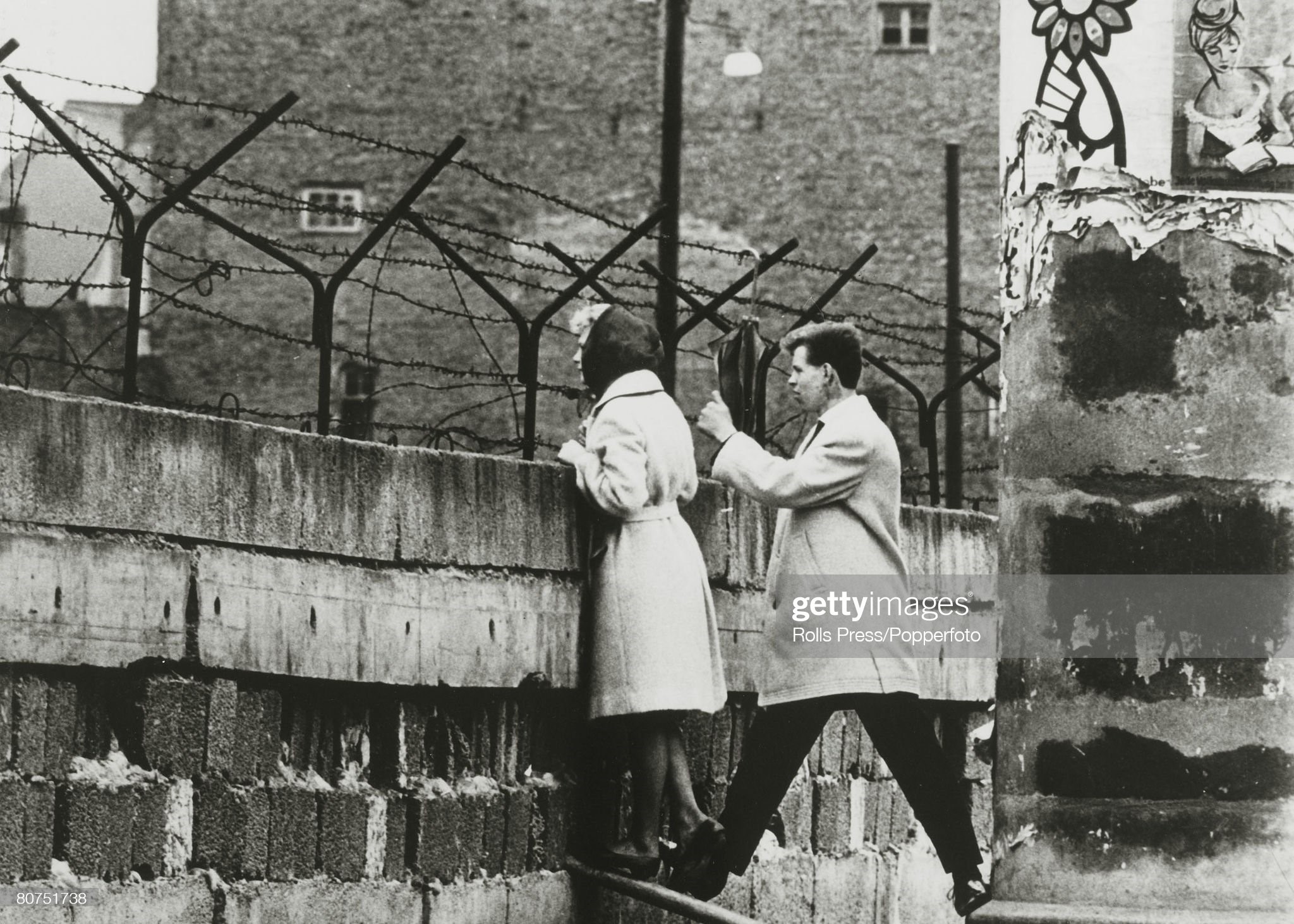 April 1962, a West Berlin girl accompanied by her boyfriend stands precariously, looking over the Berlin Wall to talk to her mother, a resident of East Berlin.