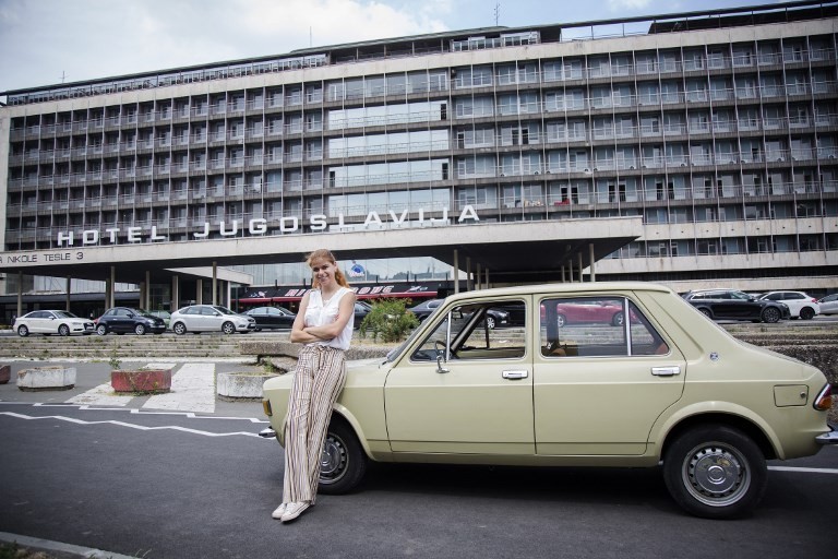 Jovana Stojiljkovic, manager of the Yugotour agency, poses for a picture on May 25, 2018 by a Yugoslav era popular car 'Zastava 101', in front of the Hotel Jugoslavija (Yugoslavia) in Belgrade.