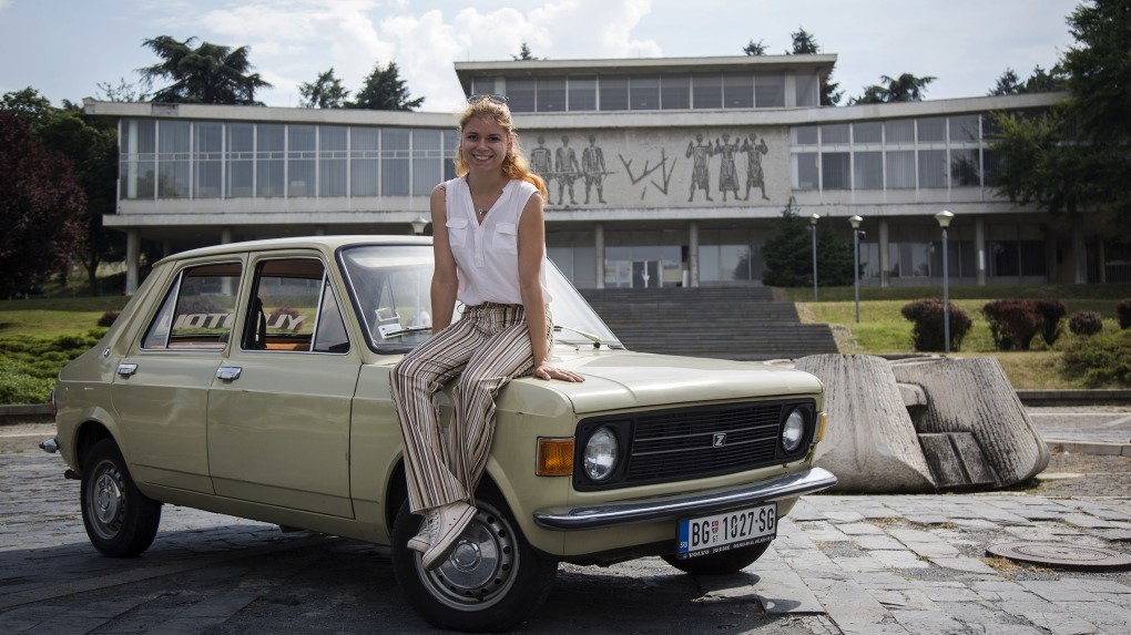 Jovana Stojiljkovic, manager of the Yugotour agency, poses for a picture on May 25, 2018 by a Yugoslav era popular car 'Zastava 101', in front of the Hotel Jugoslavija (Yugoslavia) in Belgrade. 