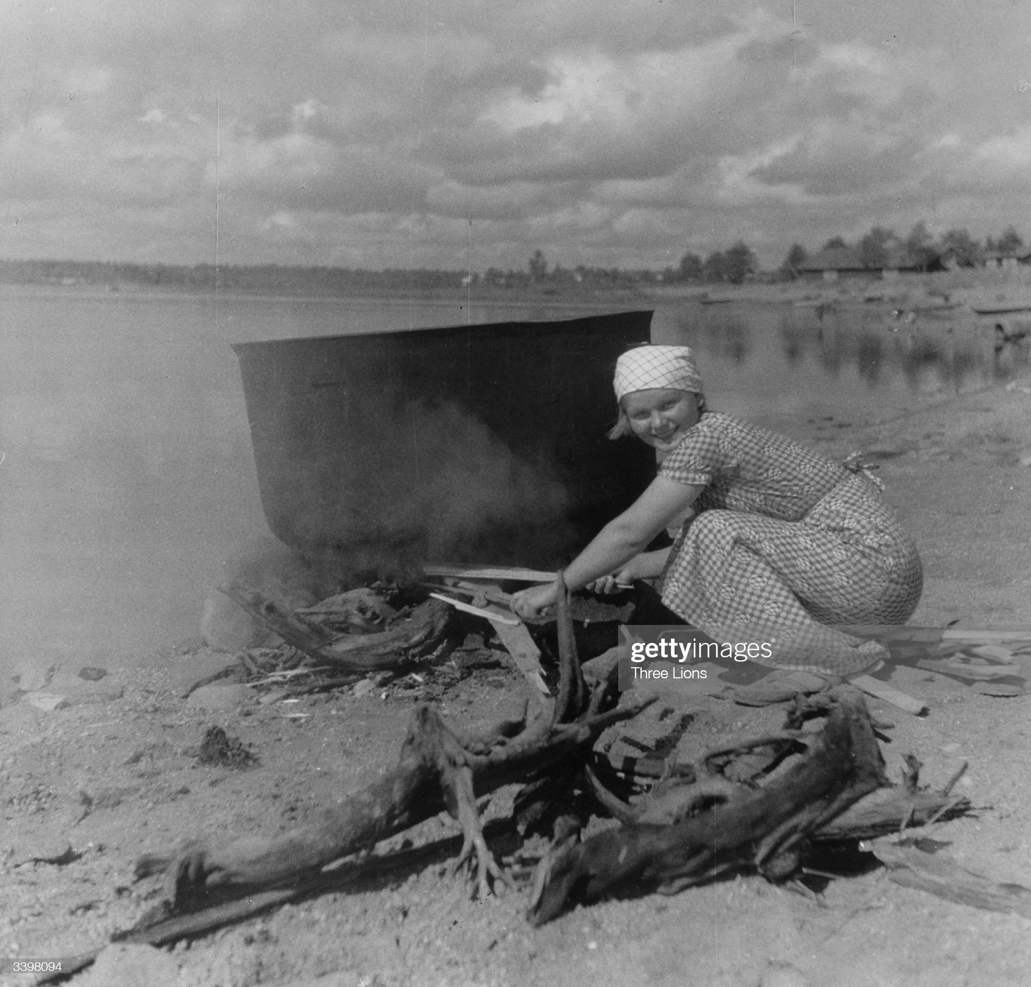 Circa 1955: a young woman tends a large cooking pot on the beach at Lavansaari Island. 