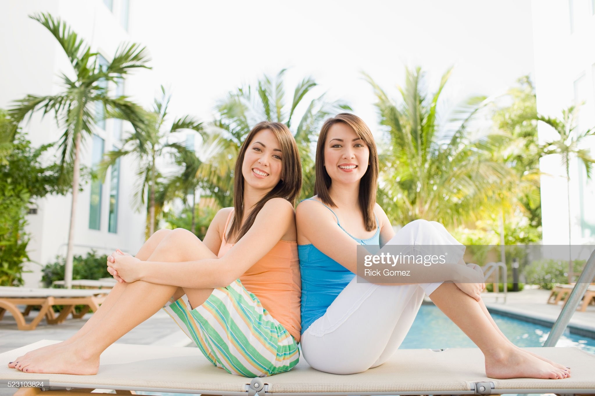 Twin sisters sitting by pool.