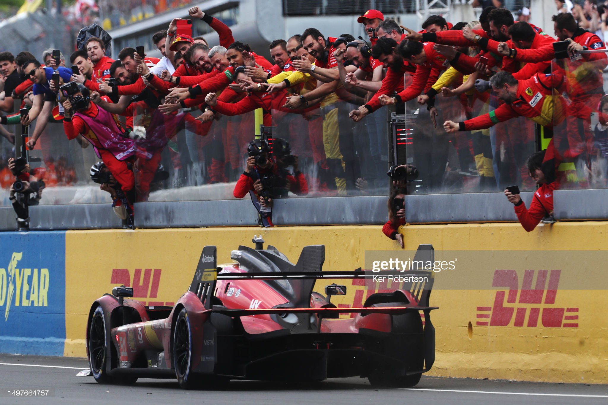 The race winning Ferrari 499P of Alessandro Pier Guidi (driving), James Calado and Antonio Giovinazzi passes celebrating team on the pit wall at the finish of the 100th anniversary 24 Hours of Le Mans race at the Circuit de la Sarthe on June 11, 2023 in Le Mans, France. 