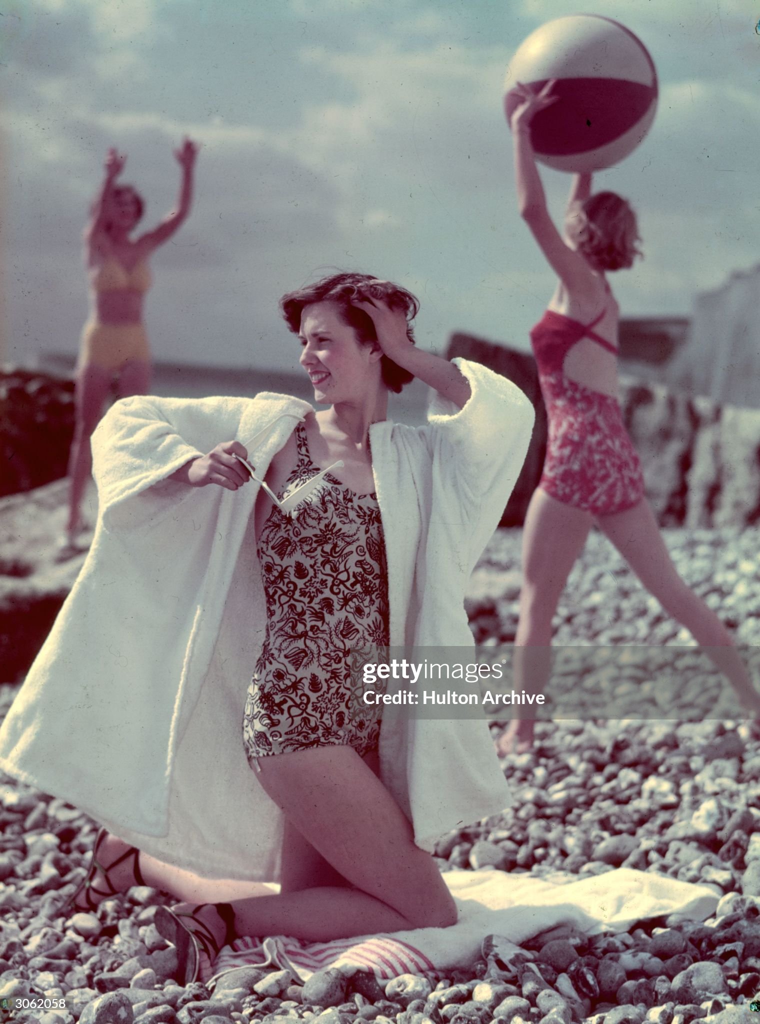 Circa 1960. A pebbly beach does not deter a group of sunbathers from their fun. 