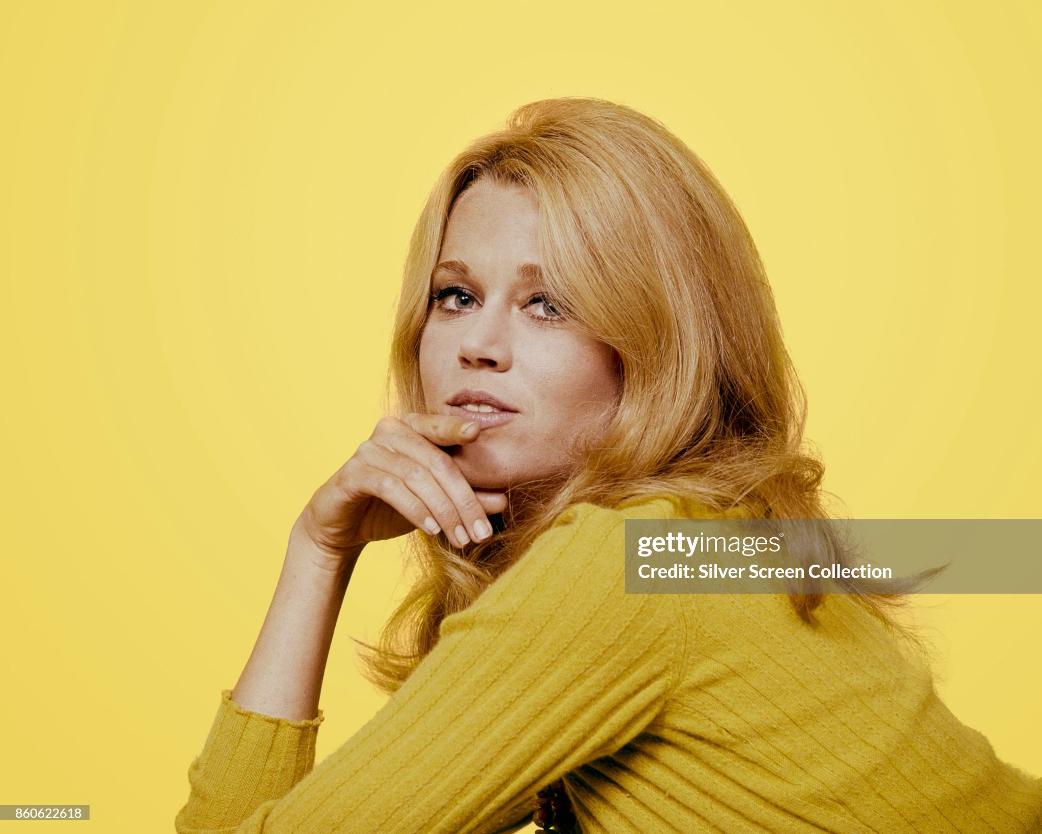 Portrait of American actress Jane Fonda, her hand on her chin, as she poses in a yellow sweater against a yellow background, 1960s. 