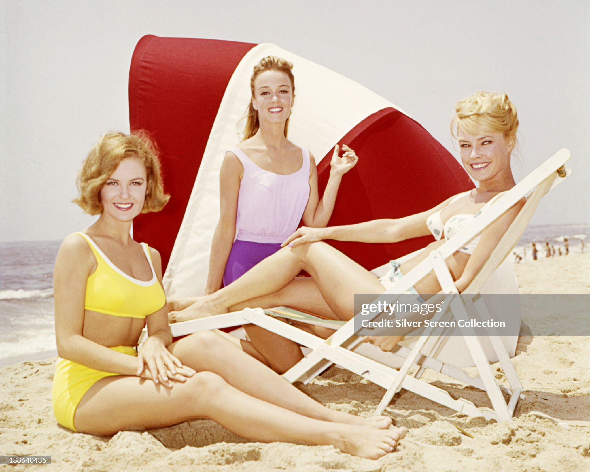 Shelley Fabares, US actress and singer, wearing a yellow bikini alongside two women in beachwear, posing on a beach, circa 1965. 