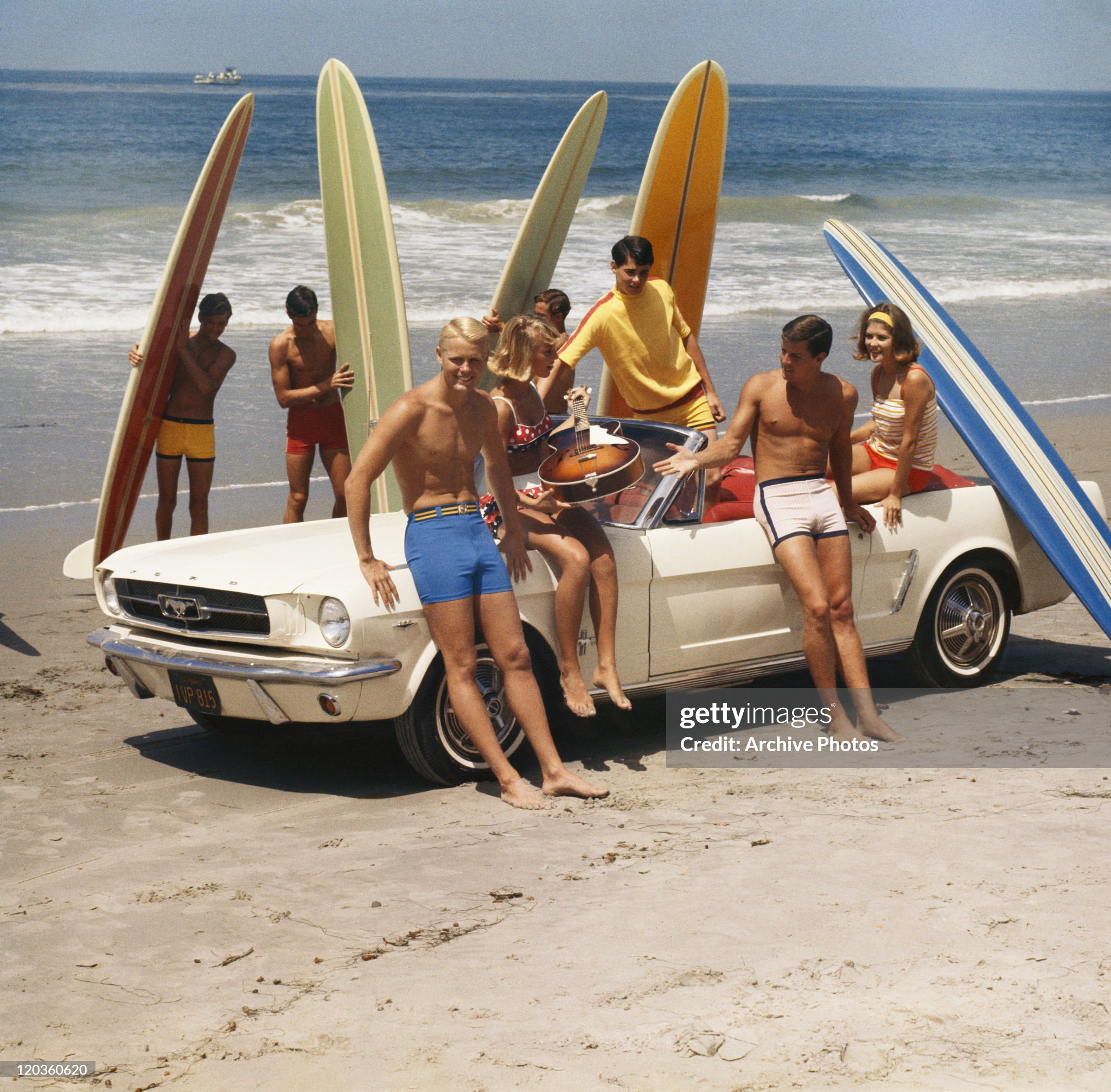 A group of surfers on a beach with a Ford Mustang car in 1968.