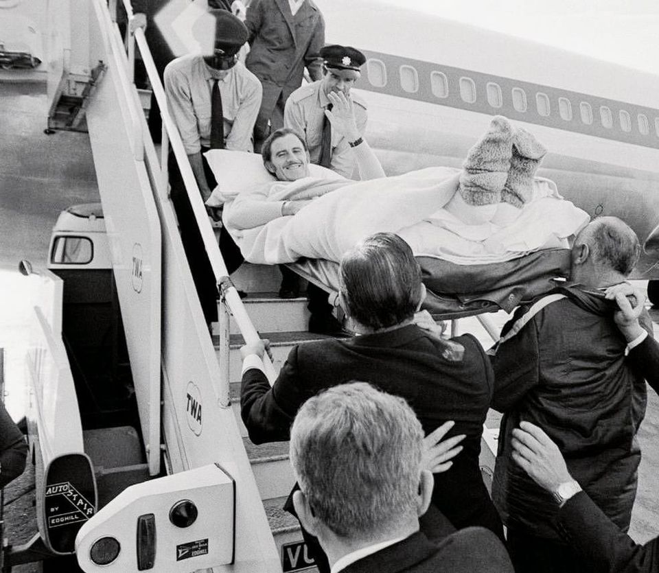 Graham Hill is carefully carried down the steps of a TWA aeroplane returning to the UK from America after crashing and breaking both of his legs at the 1969 United States Grand Prix at Watkins Glen. 