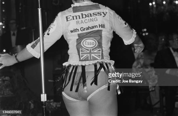 One of the 'Embassy girls' publicises the Embassy Racing team with Graham Hill in UK on 2nd December 1973. Also on her shirt is the Esso logo and a British flag. 