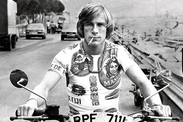 James Hunt looking mean and moody astride a motorcycle and smoking a cigarette. 