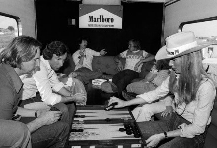 George Harrison, Beatle guitarist and F1 fan, enjoys a cigarette and a chat with race retiree James Hunt, McLaren, in the Marlboro motorhome as Jane Birbeck (right), girlfriend of Hunt, plays backgammon.
