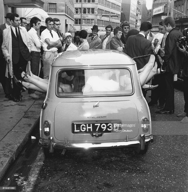 Crowd of people watch as stunts 13 mini-skirted girls managed to cram into an Austin Mini.