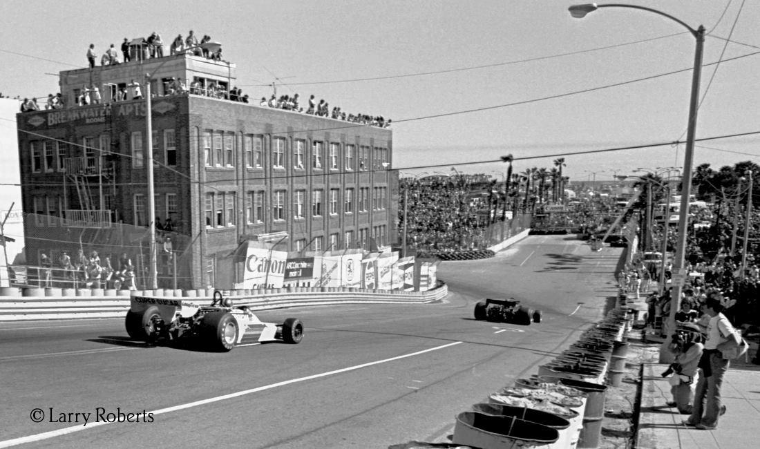 One of the trickier corners on the circuit was the first one as following the start straight a right turn would immediately throw the car into a short but sharp decline down Linden Avenue, as demonstrated here by Jody Scheckter, whose unbalanced Tyrrell has its right front off the ground. Spectators on the left enjoy the view from a building that has since been demolished.