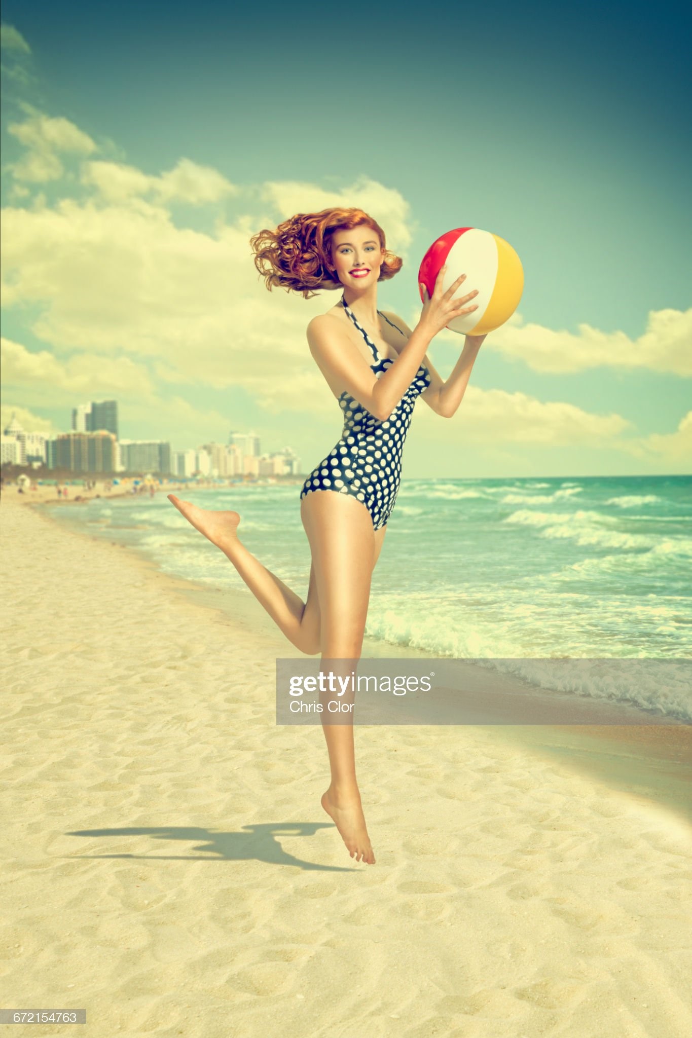 Caucasian woman running on beach carrying beach ball. 