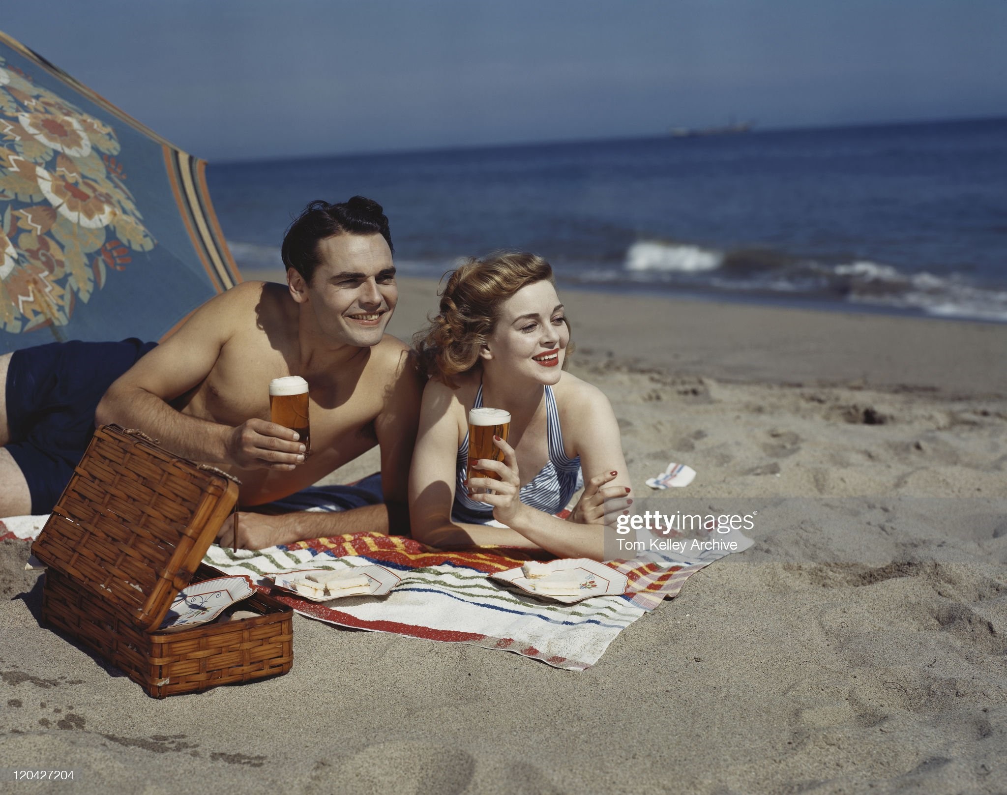 Young couple lying on beach with beer, smiling. 