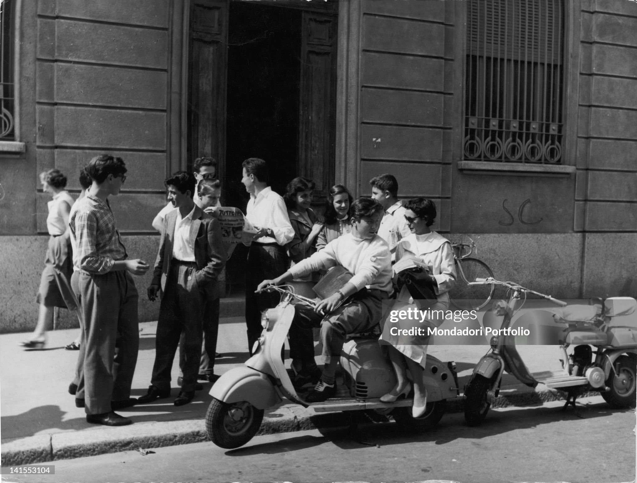A group of students, some of them on a Lambretta, chatting in front of the Liceo Berchet in Milan in the 1950s. 