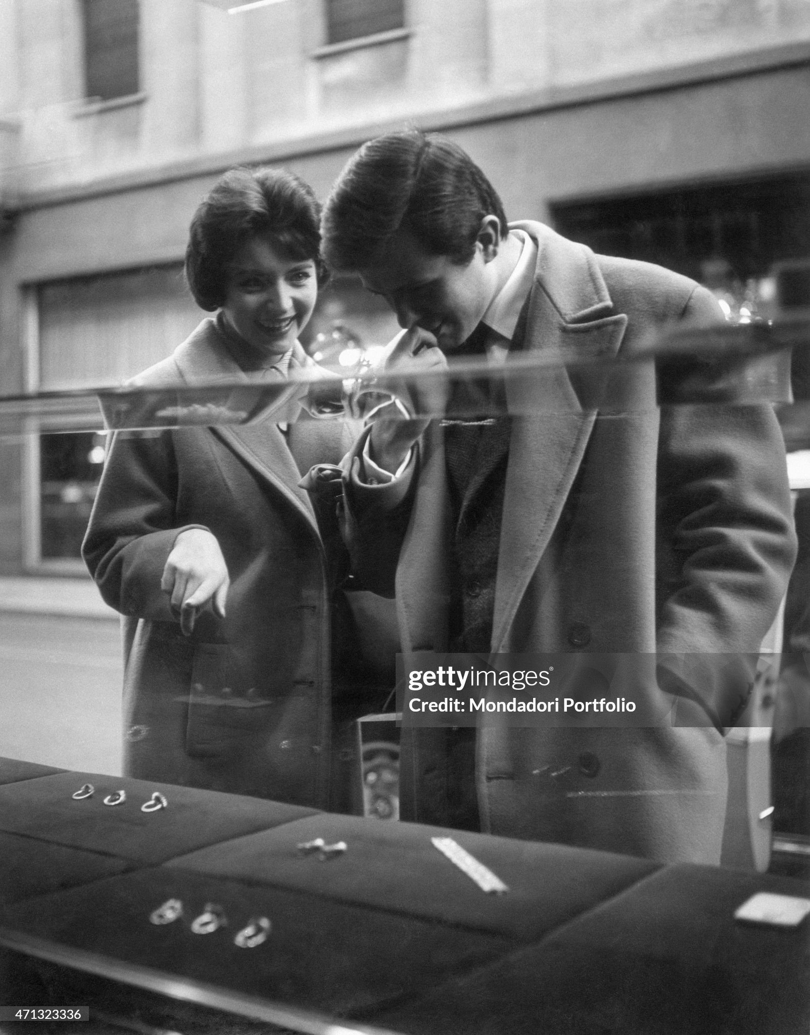 A girl showing a ring displayed in a jeweller's shop window to her partner in Milan in 1959. 