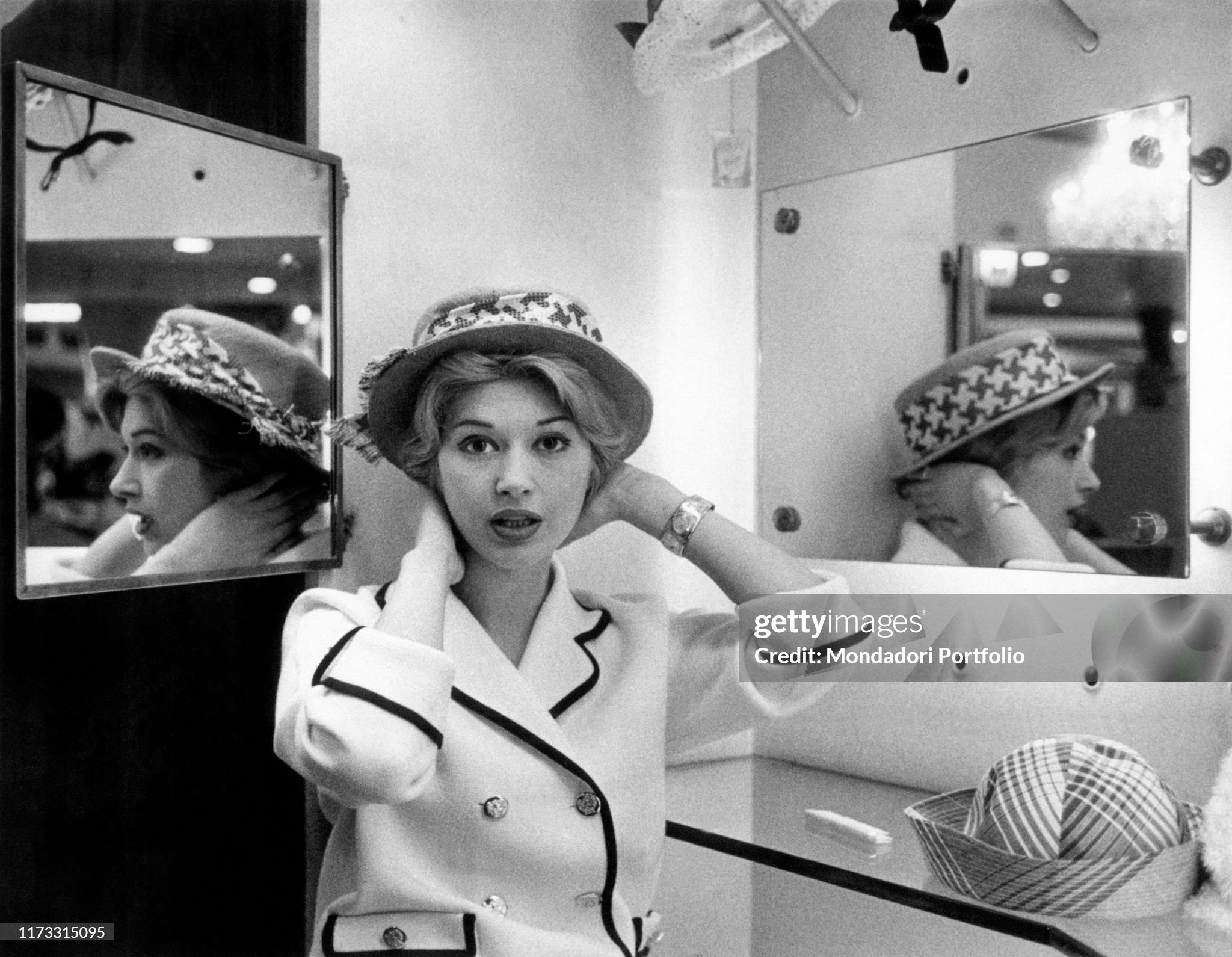 A young Italian woman trying on a hat in Milan on 01 March 1959. 