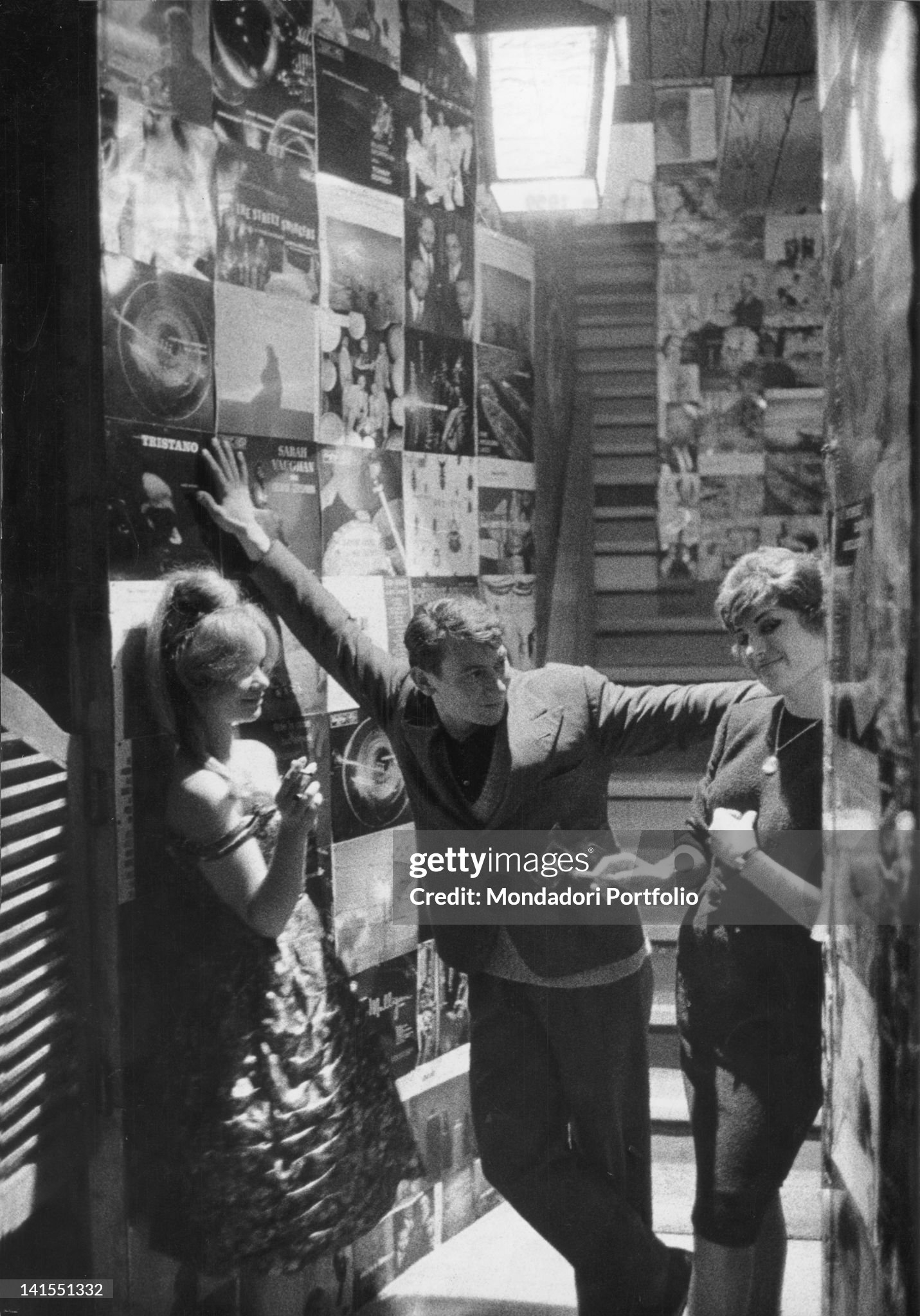 An Italian boy and two Italian girls standing in a corridor of 'Santa Tecla' nightclub in Milan on 11 December 1959. The walls are plastered over with records' covers. 