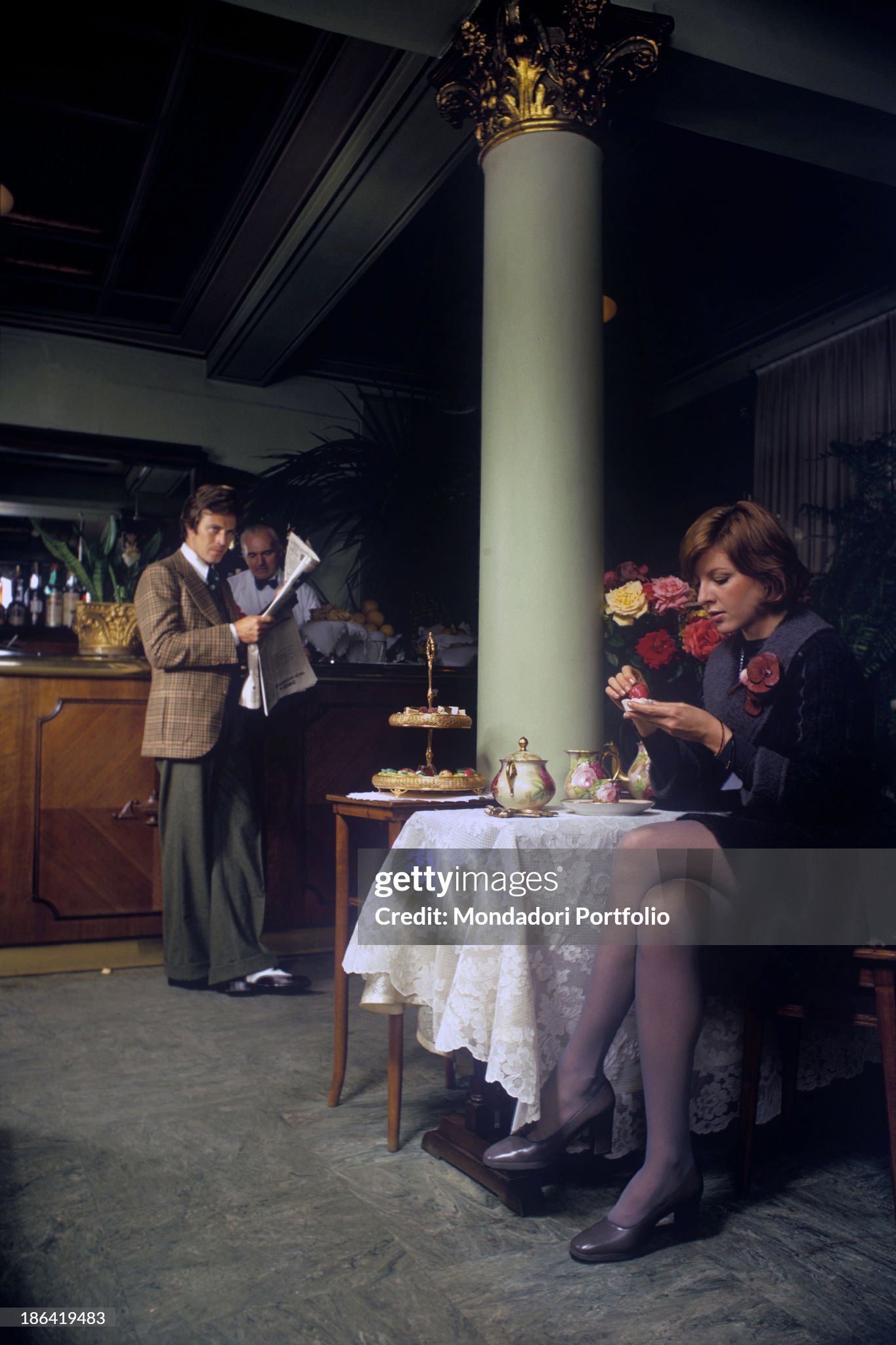 A couple sitting in a pastry shop in Milan in 1972. The woman wears a dress of Italian fashion house Krizia, the man wears a suit of Italian fashion house Cadette. 