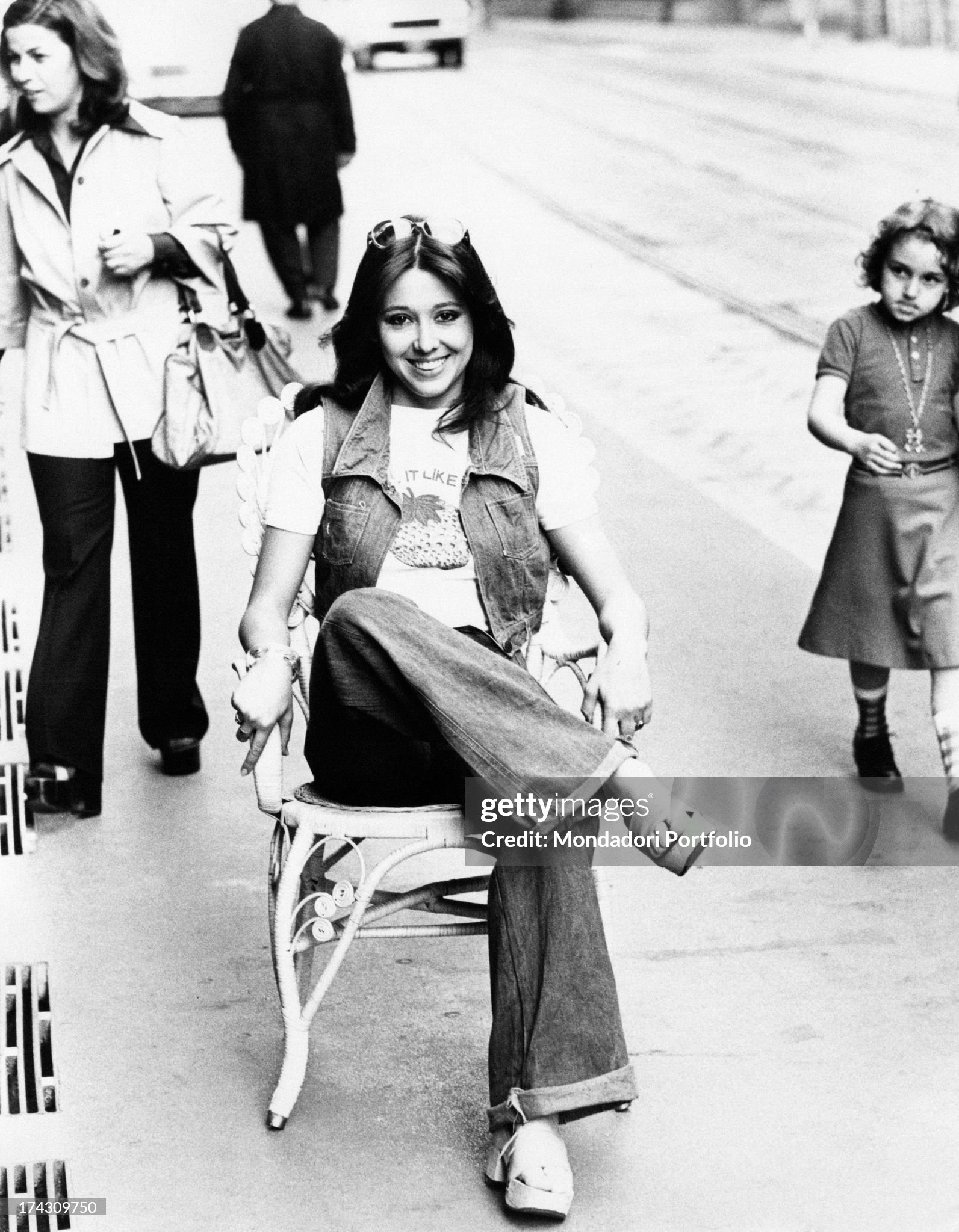 Italian showgirl Sabina Ciuffini sitting on a chair placed on the pavement in Milan in 1975. 