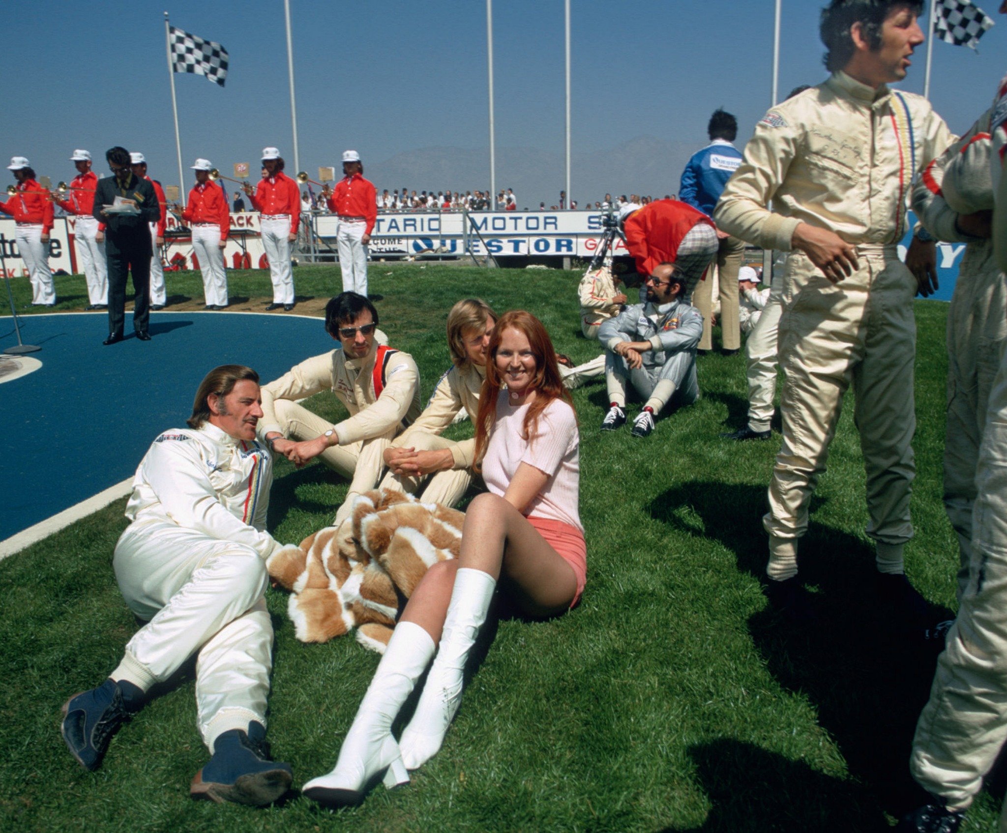 Graham Hill, Tim Schenken (with sunglasses), Ronnie Peterson (between Tim and unknown woman), Henri Pescarolo (with sunglasses, in gray jumpsuit) and Howden Ganley (standing) at the Questor Grand Prix at the Ontario Motor Speedway in California, USA, on 28 March 1971.
