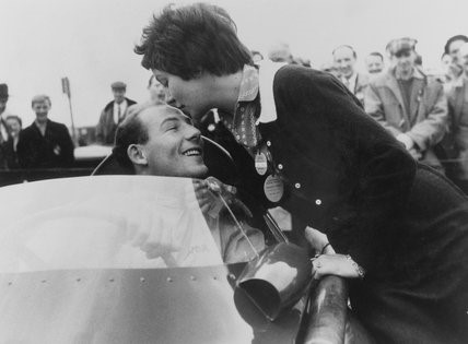 Stirling Moss, in car, kisses his fiance Katie.