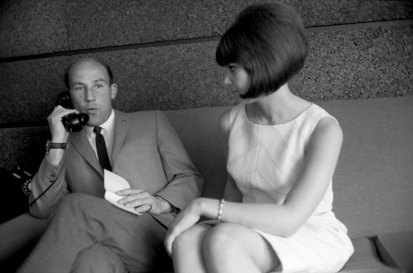 In 1964 Stirling Moss and his American wife Elaine Barberino sit on a sofa together – Stirling speaks on a telephone whilst Elaine looks at him. Elaine has a perfect beehive hairstyle and they are both dressed fashionably.