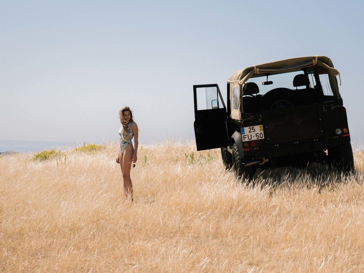 A girl in bikini in front of a Land Rover.