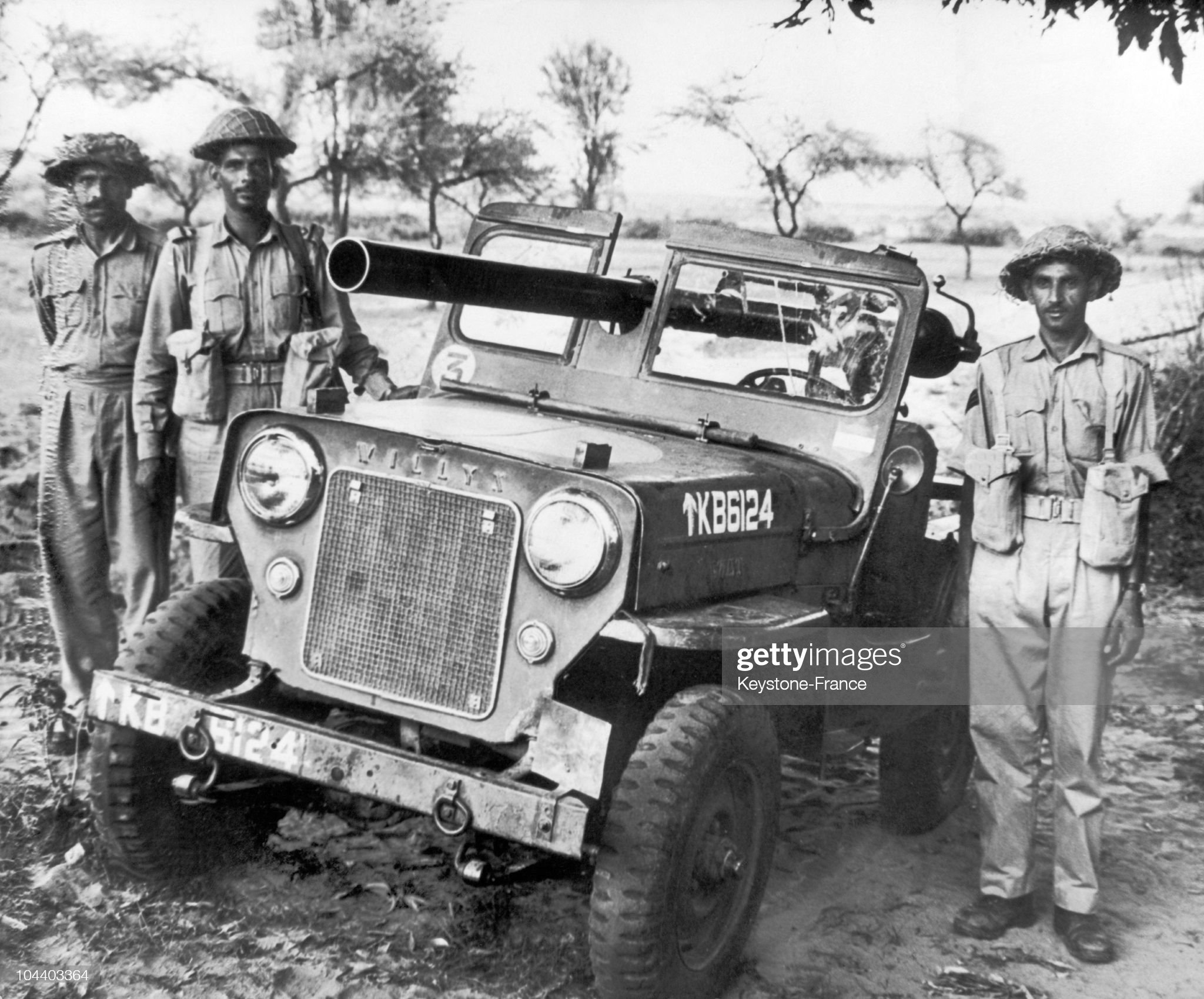 Three Pakistani soldiers surrounded a Willis Jeep equipped with a canon and abandoned by Indian soldiers.