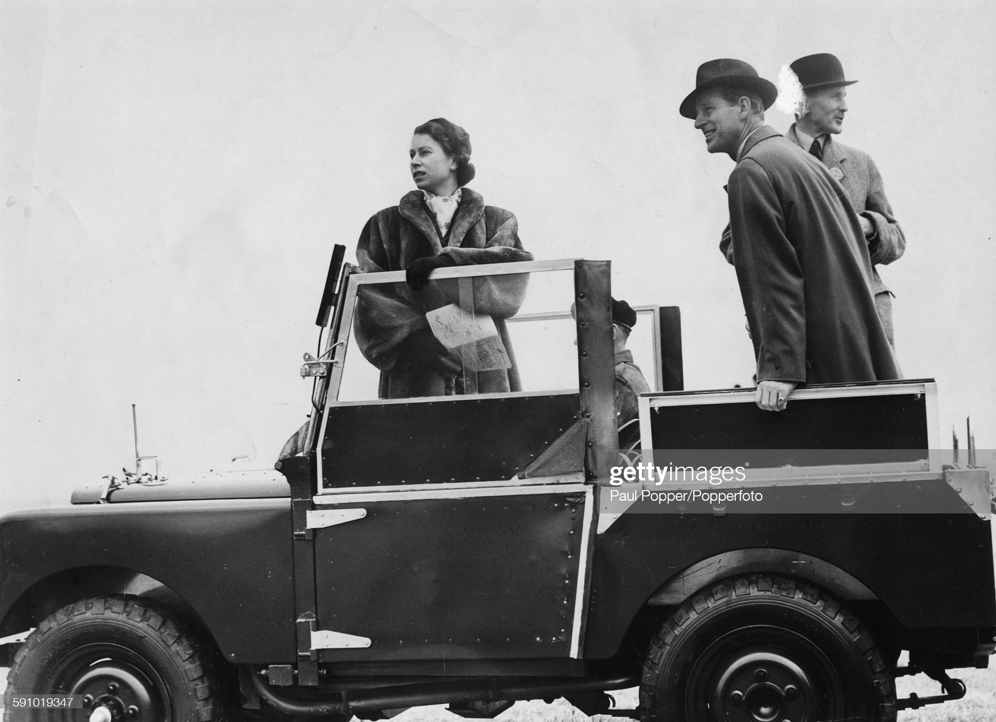 Queen Elizabeth II and Prince Philip, Duke of Edinburgh (centre), stand in the back of a Land Rover.