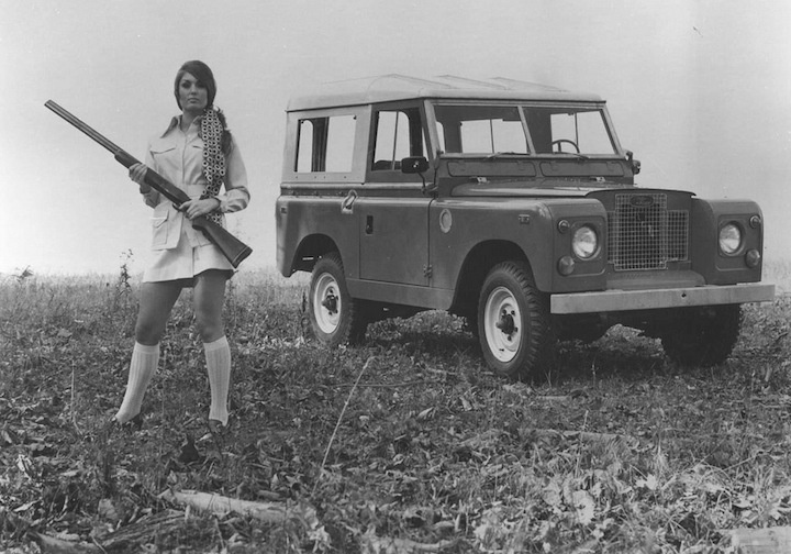 A girl with a rifle in front of a Land Rover.