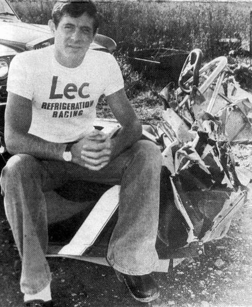 David Purley sits on the wreck of his 1977 car, after a huge crash at Silverstone. He is channeling Ronnie Peterson in his choice of outfit tight t-shirt, flares and clogs.