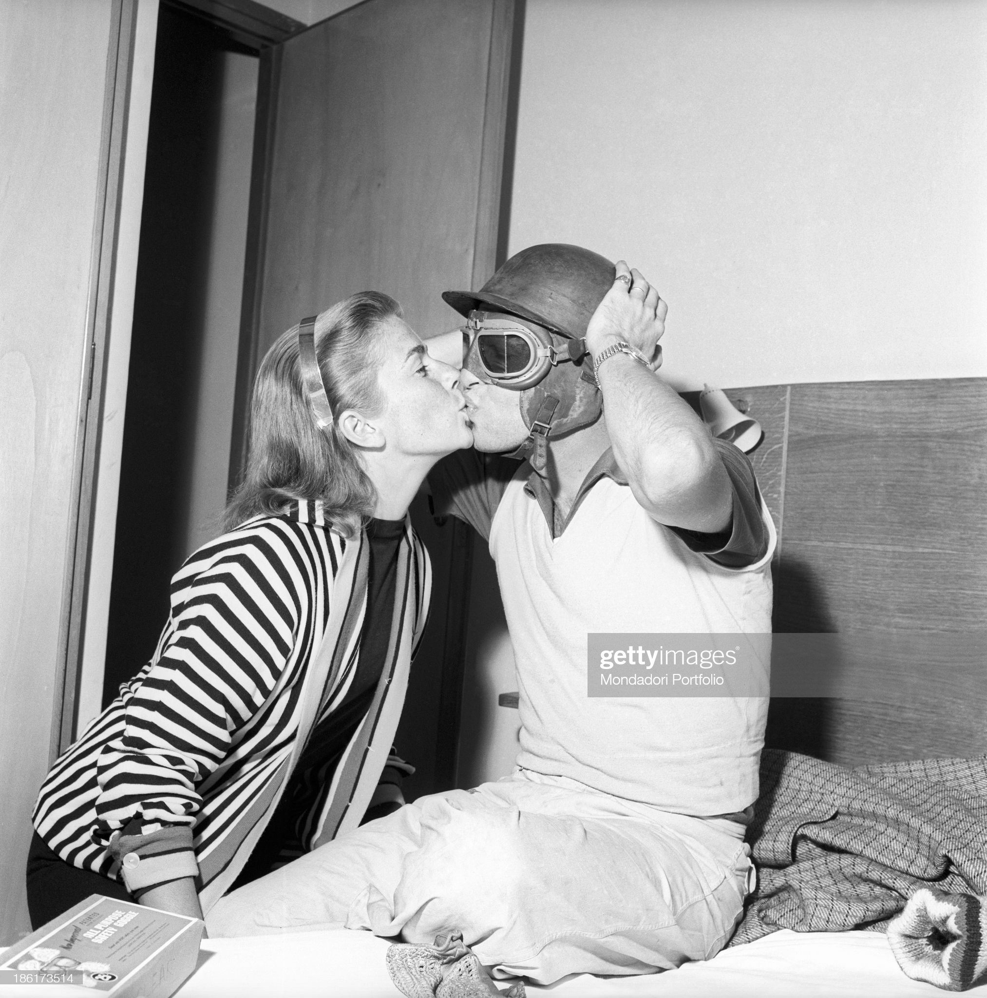 Peter Collins wearing crash helmet and racing goggles and kissing his American wife Louise Collins.