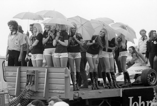 The JPS girls enjoy watching the podium from a track with the winning McLaren M23 of Peter Revson at the British GP in Silverstone on July 14, 1973.