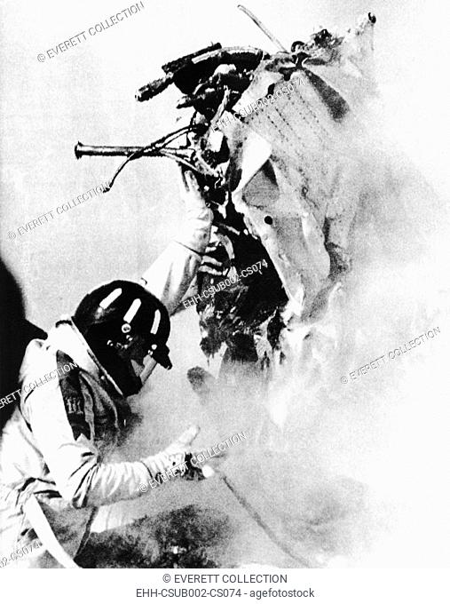 Graham Hill lifts part of the burning wreckage to clear unconscious Peter Revson on March 22, 1974. 