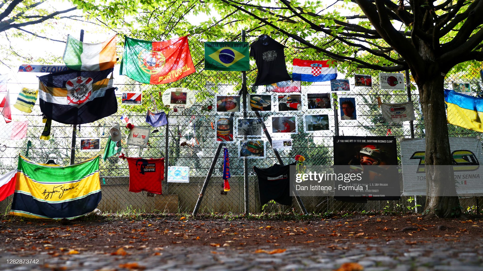 Flags and tributes hang from the perimeter fence next to Ayrton Senna's memorial near the Tamburello corner.