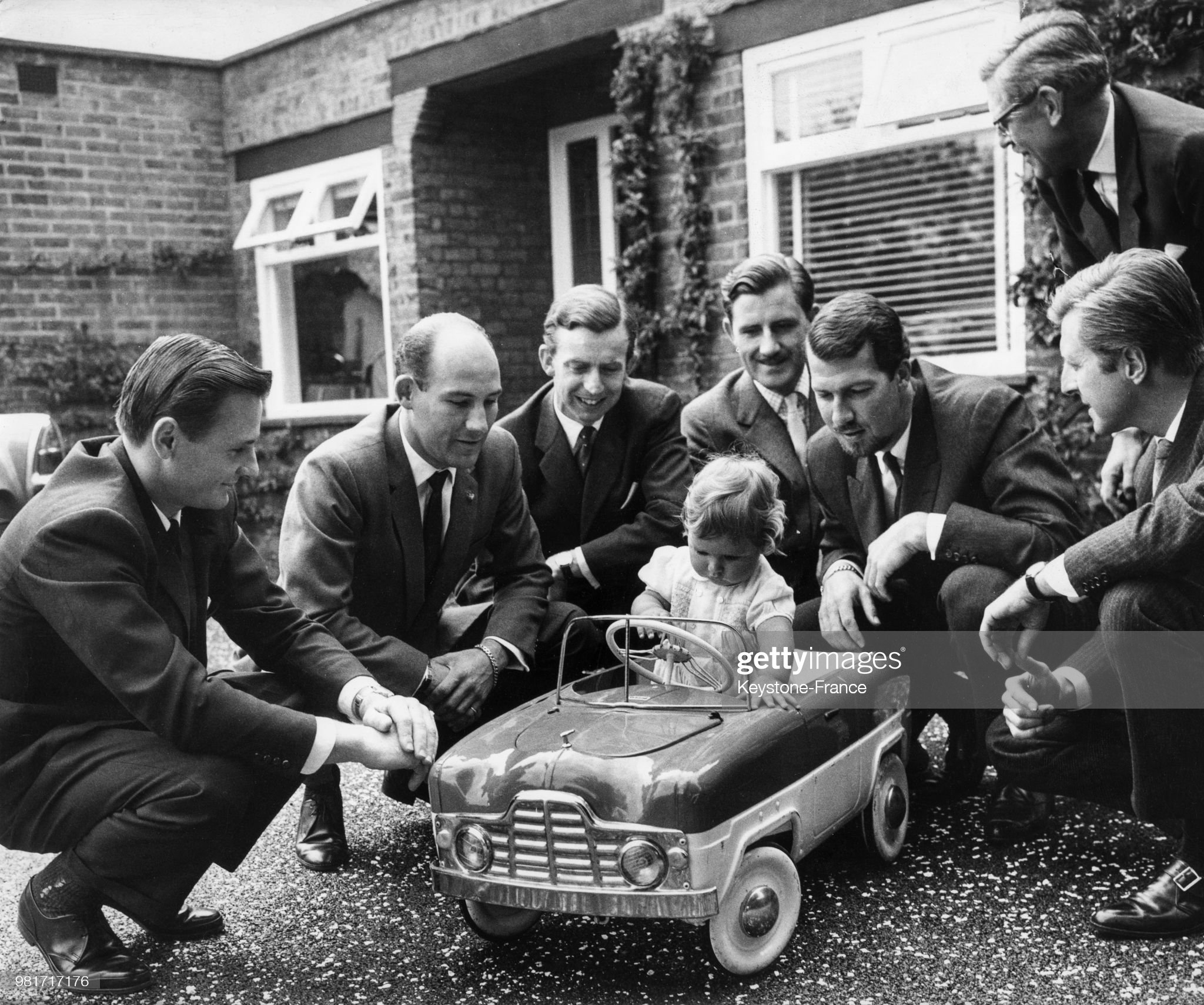 Damon Hill, 10 months old, on the day of his baptism driving a miniature car surrounded by Bruce McLaren, Stirling Moss, Tony Brooks, Graham Hill, Joakim Bonnier and Wolfgang von Trips.