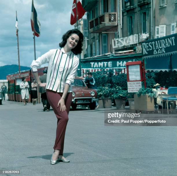 Model Chris Gregg in mauve trousers and a green and mauve ribbon-trimmed blouse on a street in St Tropez, circa 1961.