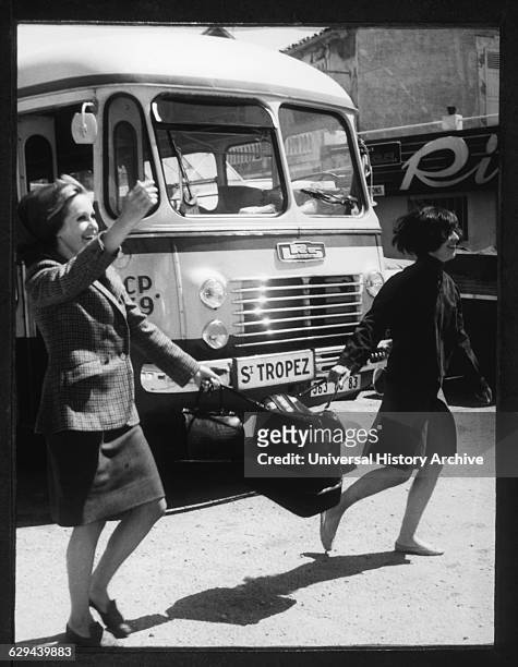 Women crossing street carrying a suitcase in St. Tropez, France, in 1965. 