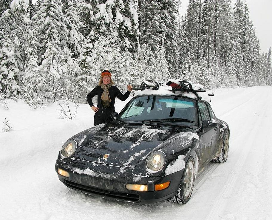 A woman and a black Porsche Carrera 4 on the snow.