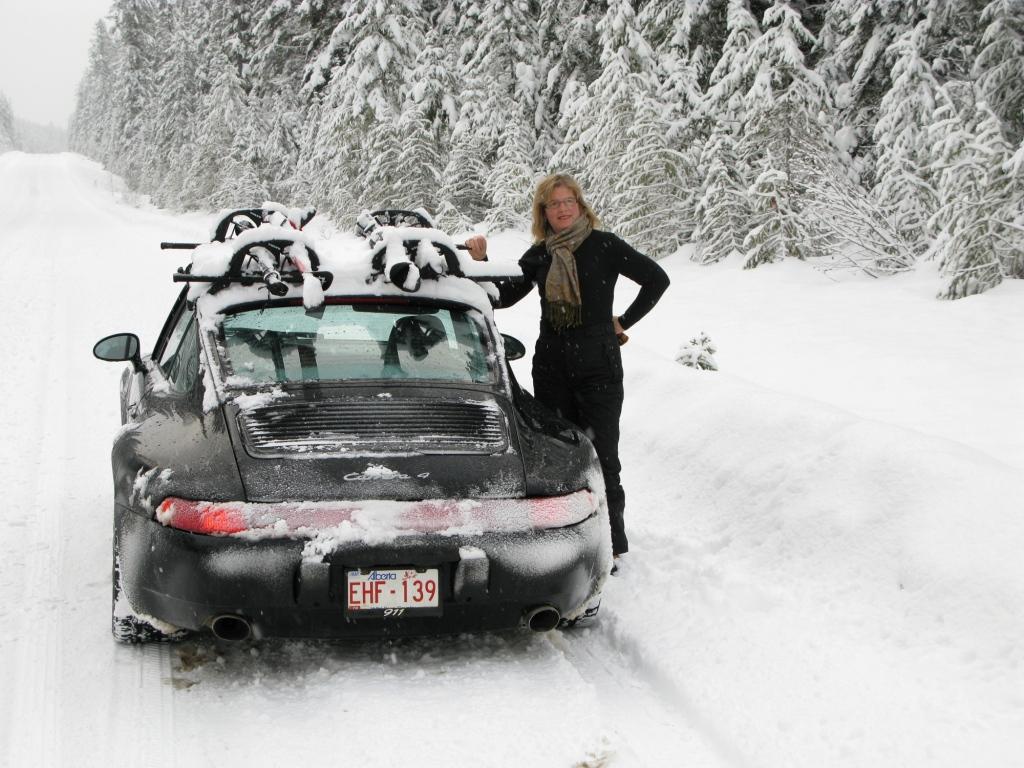A woman and a black Porsche Carrera 4 on the snow.