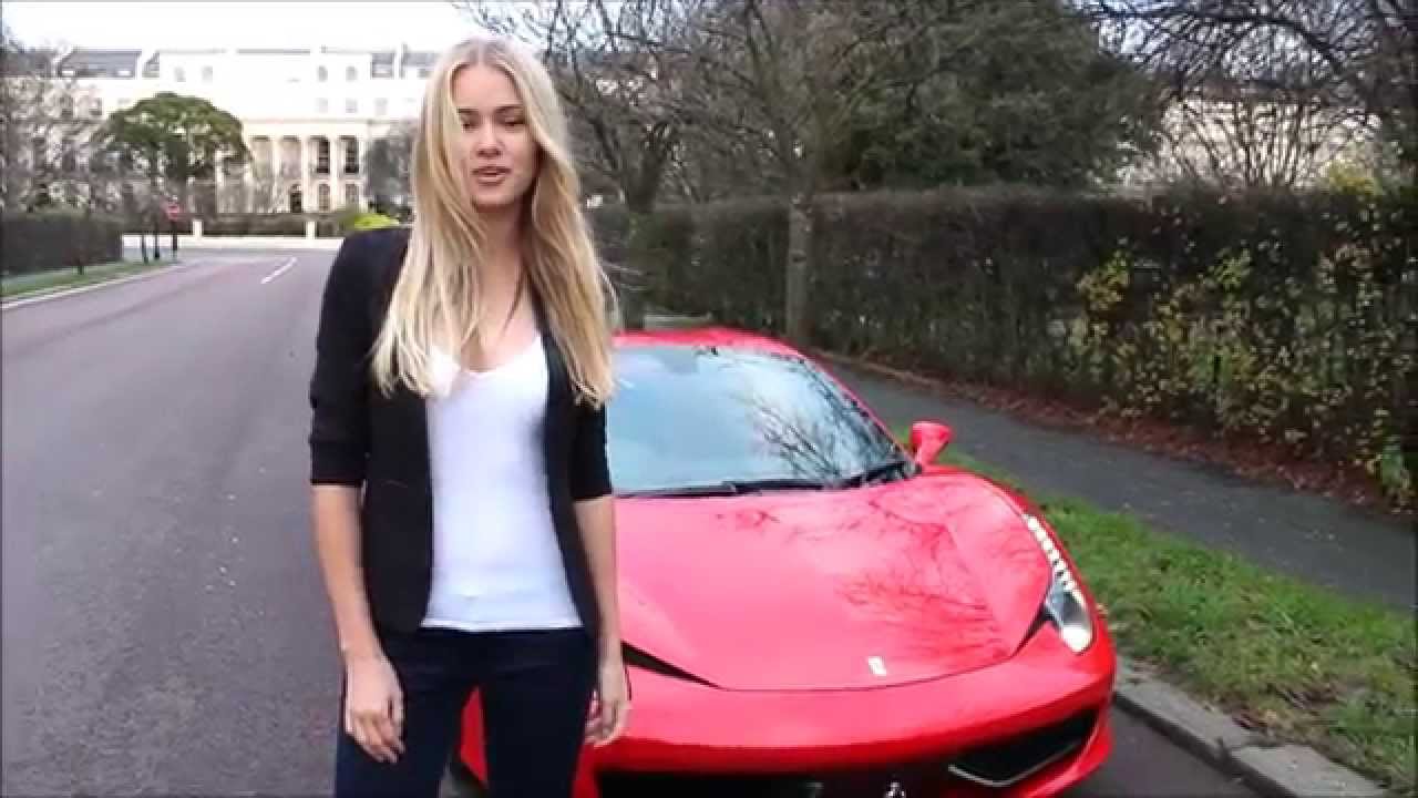 A blonde girl in front of a red Ferrari.