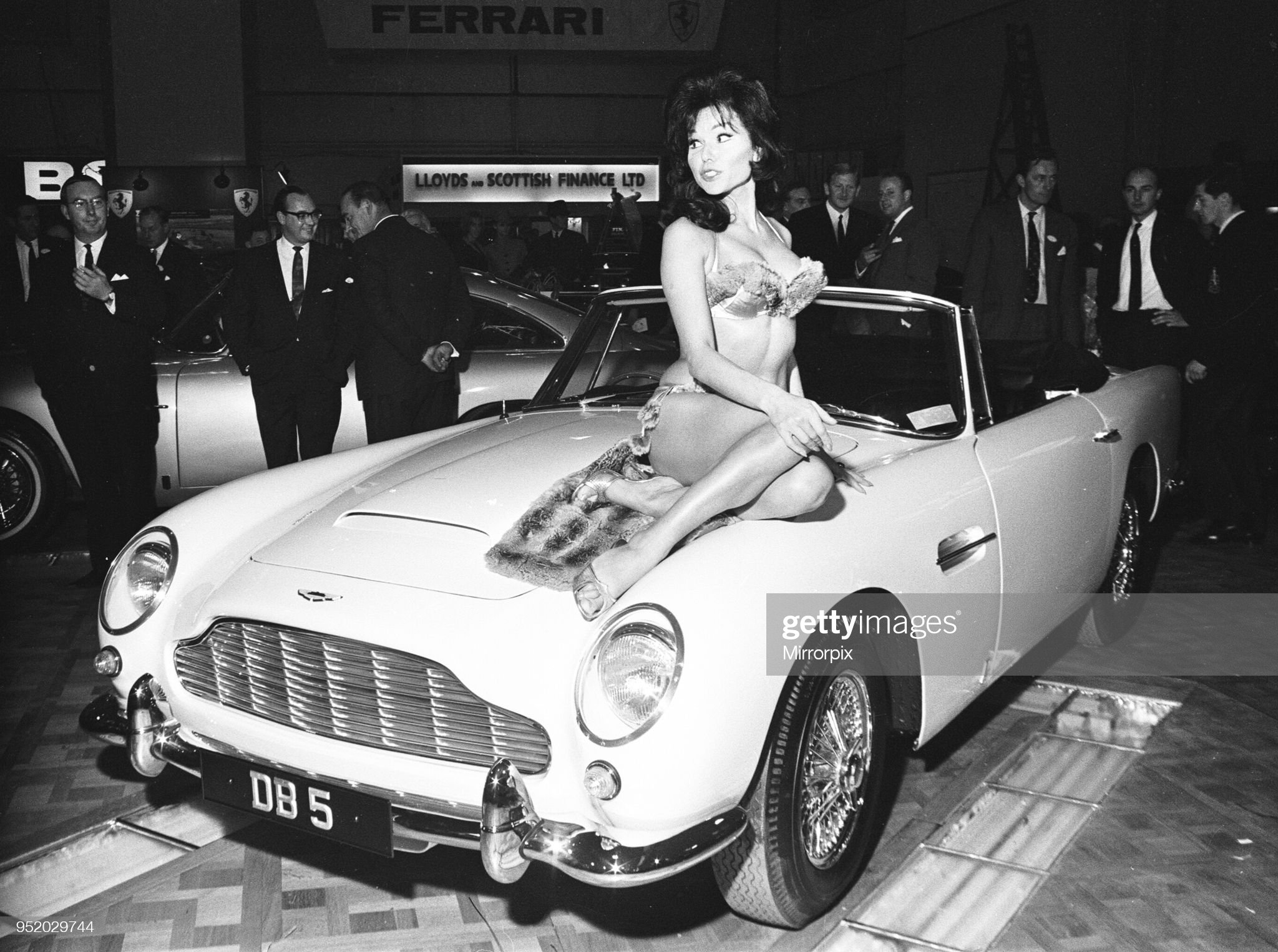 Model drapped over the bonnet of an Aston Martin DB5 at the British International Motor Show in London, 20th October 1964.