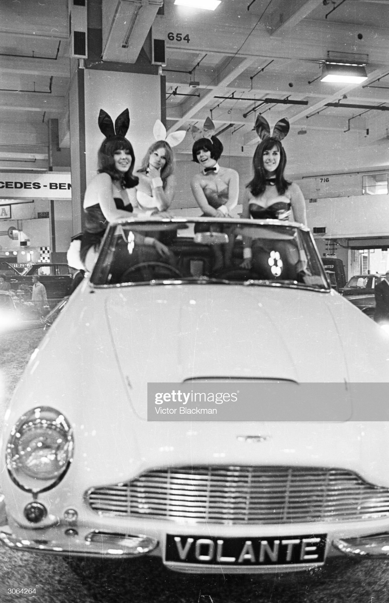 19th October 1965: a group of bunny girls sitting on an Aston Martin Volante at a motor show at Earl's Court. 